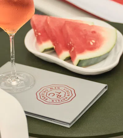 Glass of rose wine, plate with watermelon slices, pink cocktail, and menu on outdoor green table.