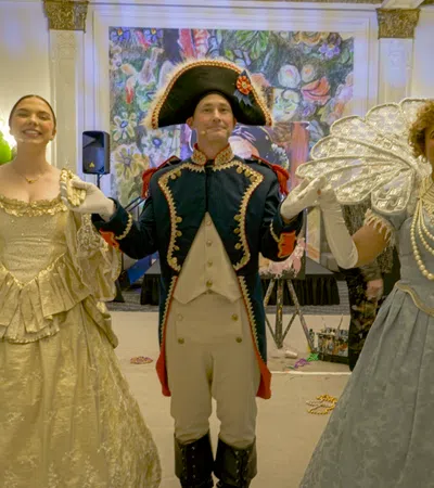 Three individuals in historical costumes pose elegantly at a vibrant event space.