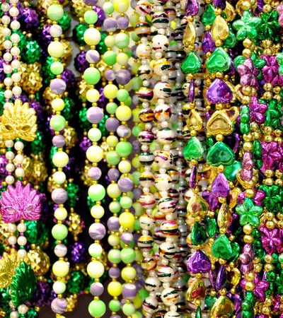 Colorful Mardi Gras beads in purple, green, gold, and yellow with various shapes and designs.