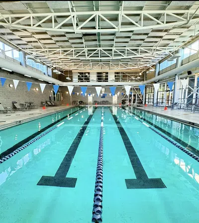 Indoor swimming pool with clear lanes, flags, deck chairs, and large windows letting in natural light.