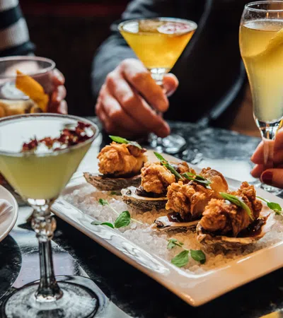 People enjoying fried oysters, cocktails, and fries on a table in a social dining setting.