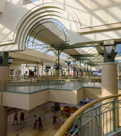 Spacious bright shopping mall interior with glass ceiling, columns, railings, and people walking below