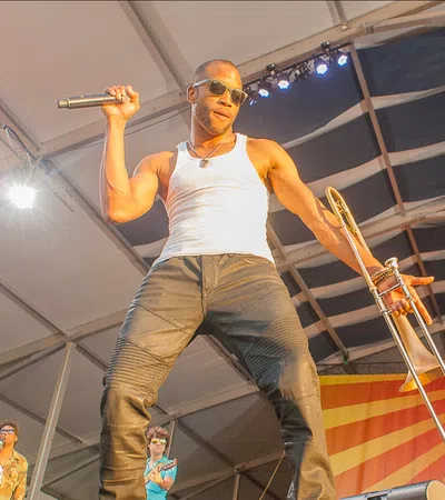 Energetic male musician on stage holding microphone and trombone under bright lights during live performance