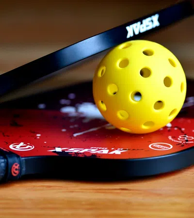 Two red XSPAK pickleball paddles crossed with a yellow perforated pickleball on a wooden surface.