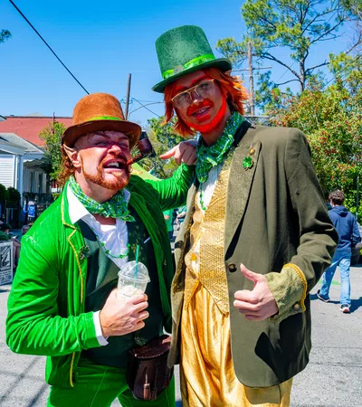 Two men dressed as festive leprechauns in green and gold costumes during a street celebration