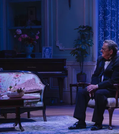Theater scene with four actors in vintage attire on an elegant living room stage set with blue lighting.