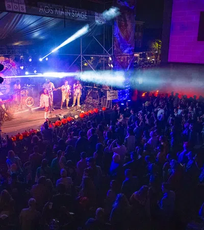 Live band performing on AOS Main Stage with colorful lights and large crowd at night concert event.