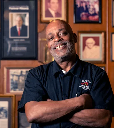 Smiling man with folded arms standing in front of a wall covered with framed vintage photographs.