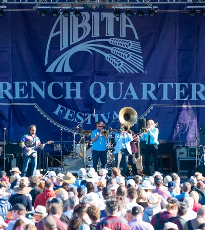 Live band performing on stage at Abita French Quarter Festival with large crowd wearing hats and colorful outfits