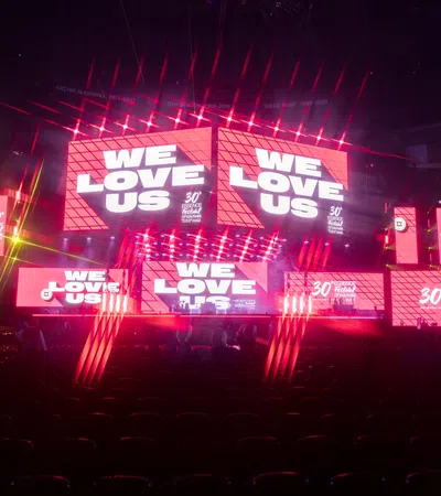 Vibrant stage setup with neon lights and large screens displaying 'WE LOVE US' at a lively event.