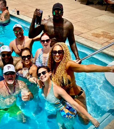 Group of happy adults enjoying drinks and fun in a sunny outdoor swimming pool party.