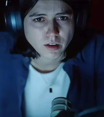 Close-up of a serious young woman wearing headphones speaking into a microphone in a dark room.