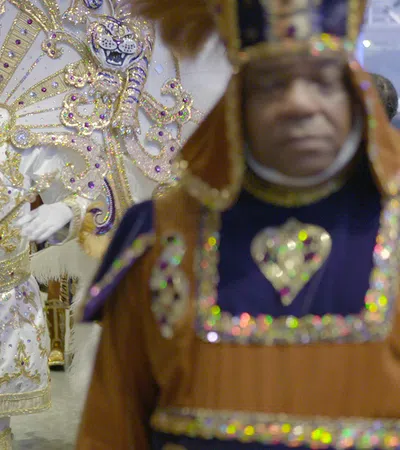 Group of men in vibrant, ornate costumes with gold, white, and purple details at a festive parade