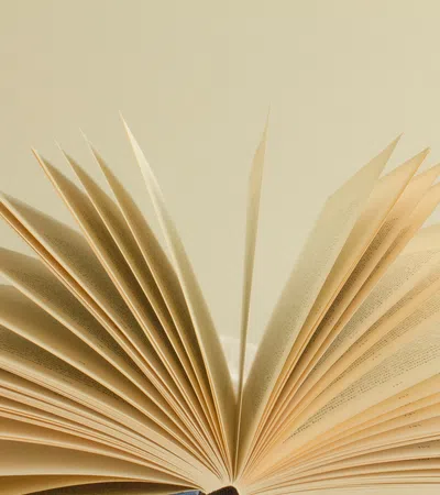 Open book with pages fanned out against a neutral beige background in soft natural light