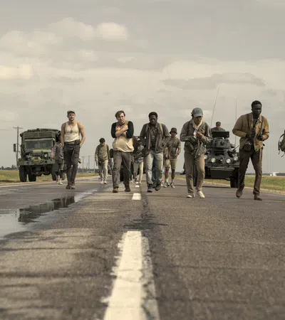 Group of diverse people walking on a rural road with military vehicles under cloudy skies
