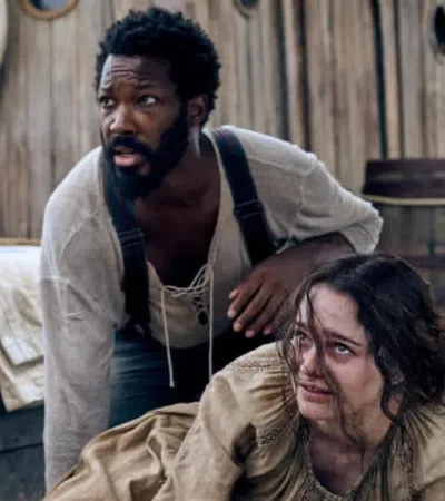 a man sitting on a bed with another man standing behind him