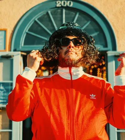 a man wearing sunglasses and a red jacket with his hands up
