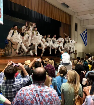 Traditional Greek dancers performing on stage in front of a large audience capturing the lively cultural event.