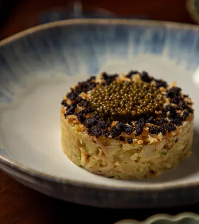 Gourmet dish with finely chopped ingredients topped with black and golden caviar on a ceramic plate.