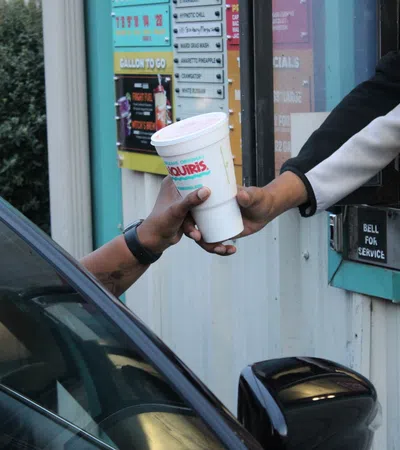 Drive-thru service handing a large White Castle drink cup to a customer in a black car at the ordering window