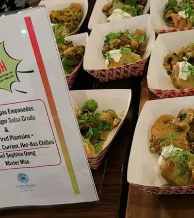 Multiple servings of chorizo with plantains and salsa in paper trays beside a sign detailing the hot dish ingredients.