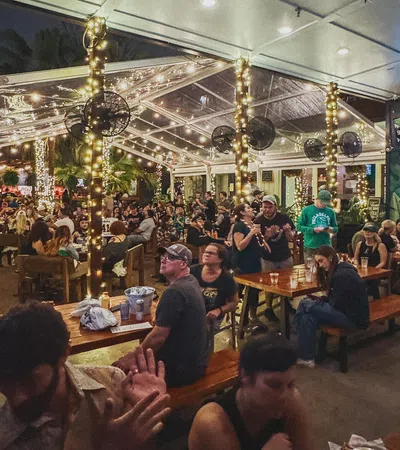 Crowded outdoor bar patio with string lights and people socializing under a transparent roof at night
