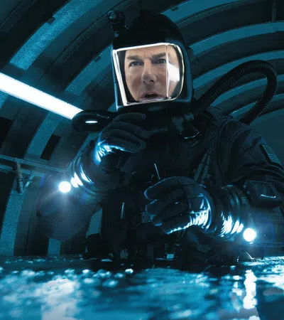 Man in black diving suit and helmet prepares underwater equipment in a dimly lit tunnel.