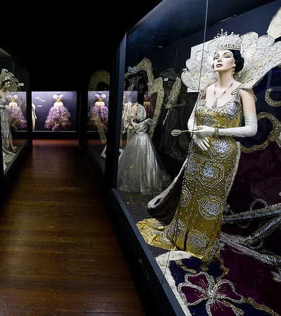 Museum display of elegant vintage mannequins dressed in ornate beaded gowns and royal accessories in glass cases.
