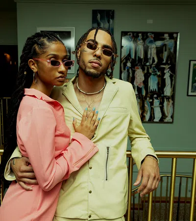 Stylish couple posing in trendy outfits indoors with art in the background.