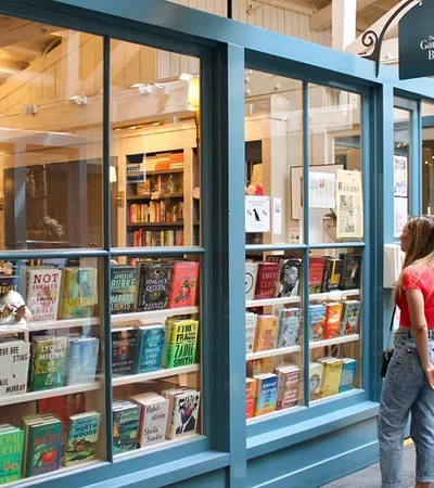 Couple browsing books displayed in the window of a cozy independent bookstore with blue framing inside a wooden building