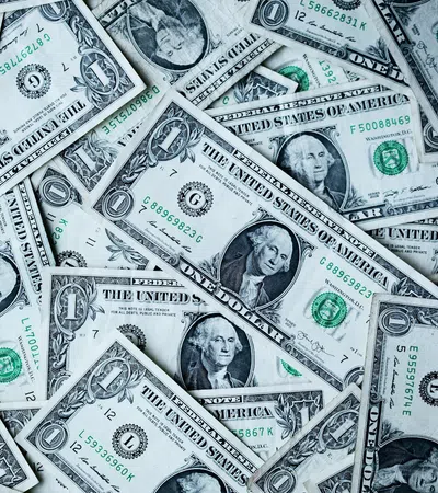 Multiple one dollar US banknotes scattered, showing George Washington's portrait and currency details.