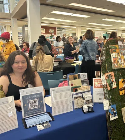 People explore informational booths at a busy community event in a well-lit indoor space with displays and artwork.