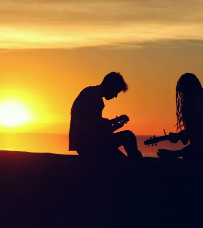 a man and woman sitting on a rock with the sun setting behind them