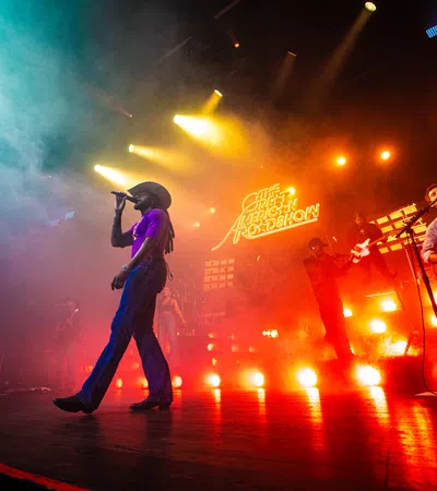 Live concert with a singer in a cowboy hat, guitarist, and vibrant colorful stage lighting and fog effects
