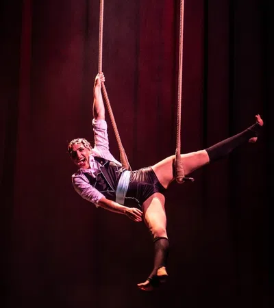 Two acrobats performing aerial stunts on ropes, with dramatic lighting and a vibrant stage backdrop.