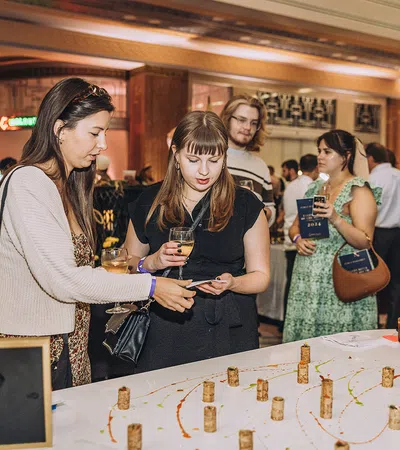 People dressed in semi-formal attire sampling wine and engaging at a social tasting event indoors.