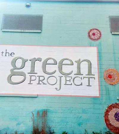 Mural on turquoise wall reading The Green Project with decorative circular mosaic art around it.