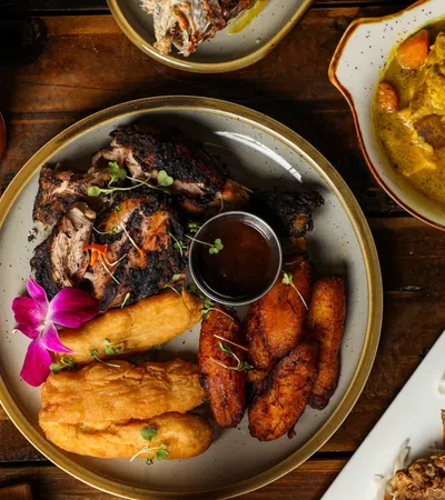 A beautifully plated Caribbean meal featuring jerk chicken, fried plantains, and a colorful side dish.