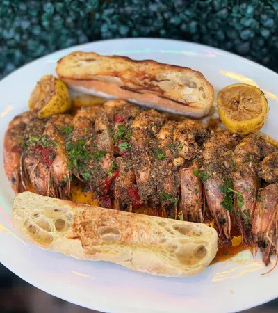 Grilled seasoned shrimp served with toasted bread and lemon halves on a white plate.