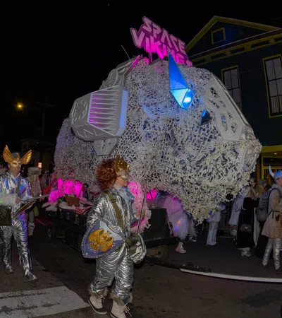 People in silver space-themed costumes parade beside a large illuminated float reading Space Vikings at night.
