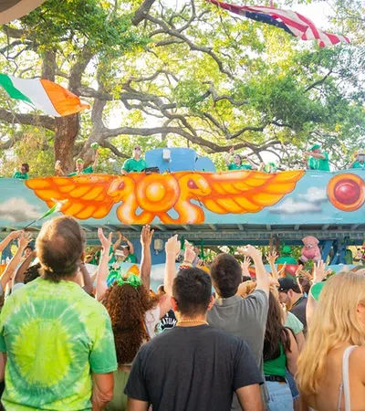 Crowd wearing green celebrates next to colorful parade float with Irish and American flags during festive event.