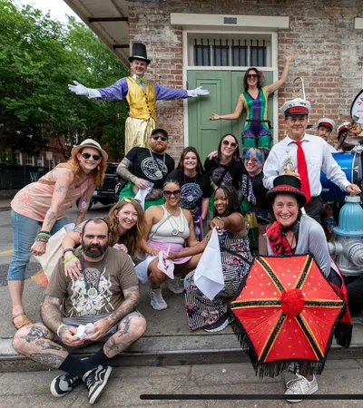 Group of diverse people and musicians posing joyfully outdoors with colorful costumes, instruments, and a decorated umbrella.