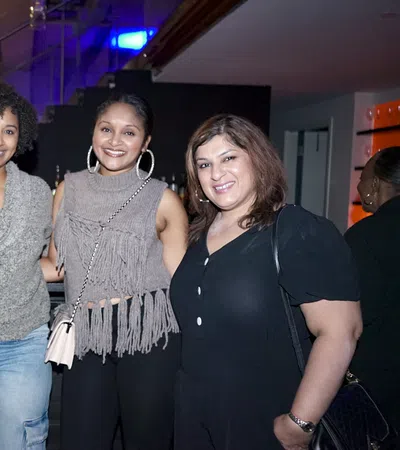 Four diverse women smiling and posing together at an indoor event with modern lighting and decor.
