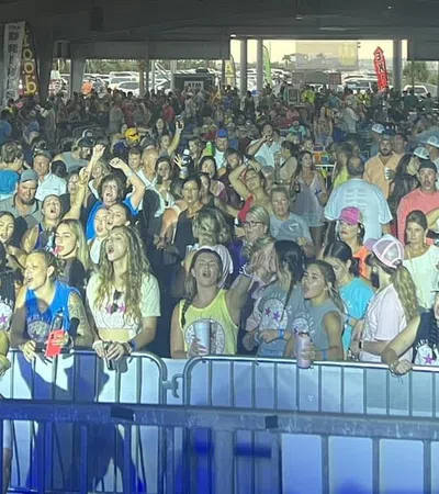 Large crowd enjoying an indoor concert or event with people cheering and taking photos under overhead lighting.