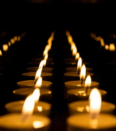 Rows of glowing tea light candles with flickering flames in a dark setting creating warm ambiance.