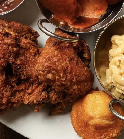 Plate with crispy fried chicken, cornbread muffin, mac and cheese, candied yams, and red beans with rice.