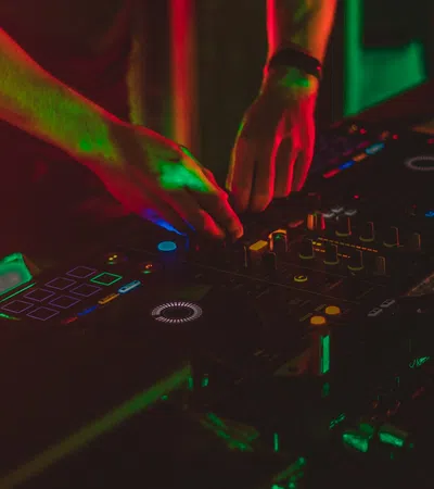 DJ mixing music on a Pioneer DJ controller under vibrant red and green club lights at night.
