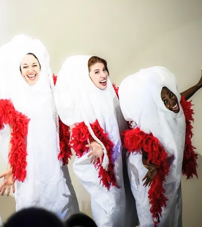 Group of four performers in creative white and red costumes, joyfully posing together on stage.