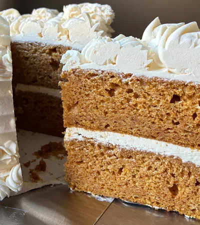 Close-up of a sliced two-layer brown cake with white frosting and decorative icing on top and sides.