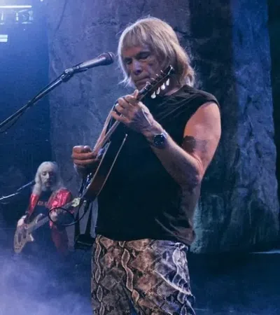 Rock band performing live on stage with guitars, piano, and dramatic lighting effects and smoke.